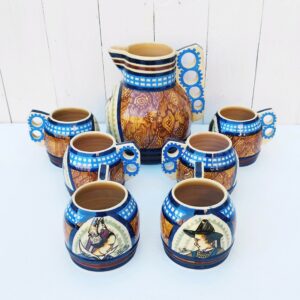 Service à cidre en faïence de Quimper par Paul Fouillen. Composé d'un pichet et six bolées. Décor de Bretonne sur le pichet et décor de trois bretonnes et trois bretons sur les bolées. Petits défauts de cuisson sur le col d'une bolée. Deux petits éclats sur le devant d'une bolée Très bon état. Hauteur pichet : 19 cm Hauteur bolée : 8,5 cm