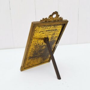 Cadre photo chevalet en laiton de style Louis XVI, une frise florale avec noeud ruban sur le haut. Traces de vert-de-gris sur l'arrière. Bon état général. Dimensions hors frise : 14 x 9,5 cm