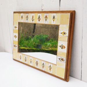 Miroir horizontal entouré de carreaux de céramique unis et à décor floral par Michel Boillot, le tout encastré dans un cadre en bois. Signé MB. Un point d'accroche sur l'arrière, quelques petites rayures sans gravité sur le miroir. Très bon état. Dimensions cadre : 36,5 x 27 cm Dimensions miroir : 25 x 15,5 cm