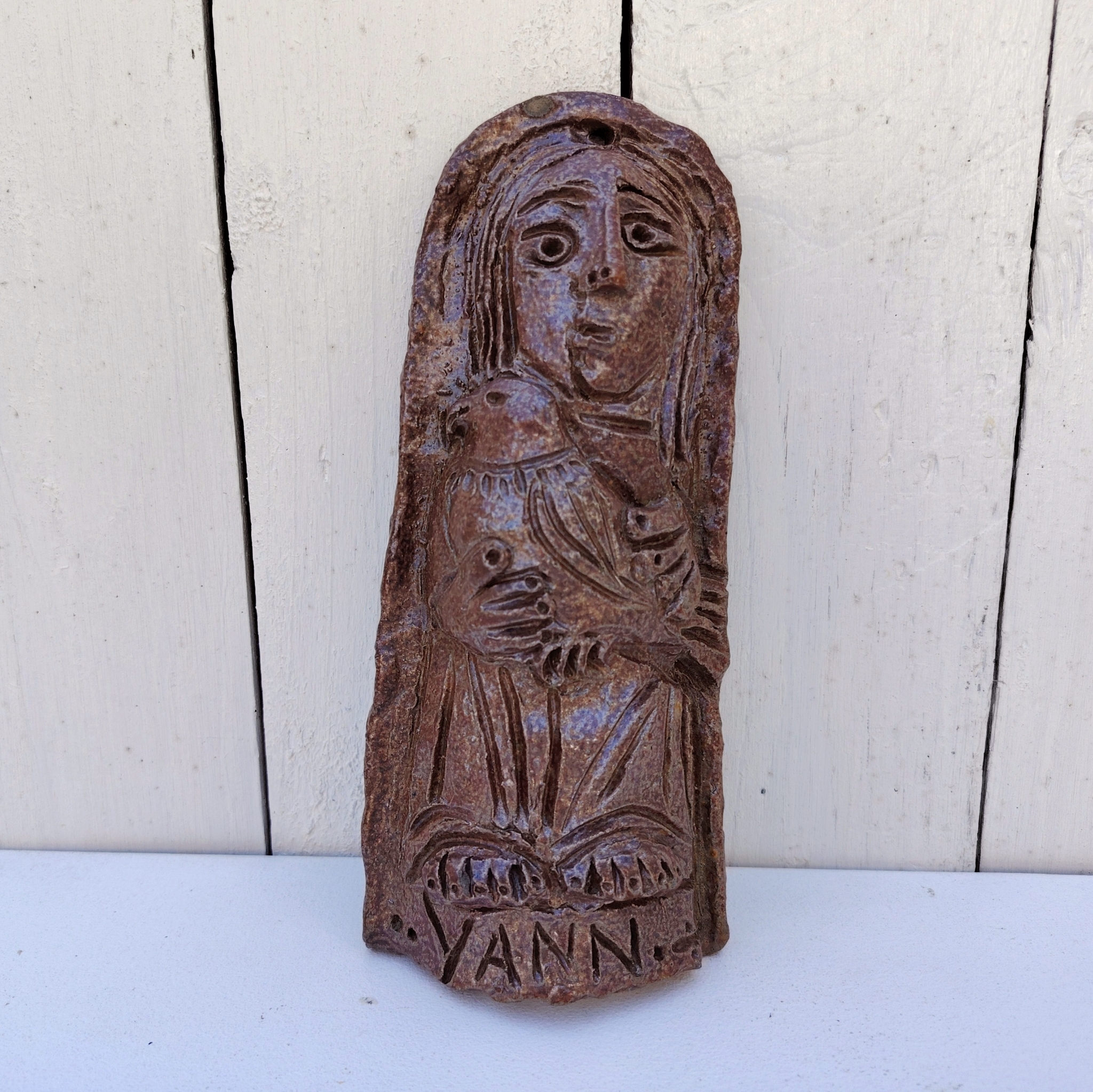 Sculpture anthropomorphe représenatnt Saint jean avec un oiseau en terre cuite vernisée, par Raymond Debiève. Un trou sur le haut pour l'accrocher au mur. Signé et daté en creux.