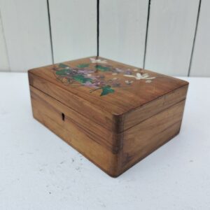 Boite à bijoux en bois verni à décor central de bouquet de fleurs, inscription Royan sur le couvercle. Capitonné en satin rose à l'intérieur Ne possède plus sa clé. Des petites rayures d'usage, Petites taches sur le capitonnage. Bon état général. Dimensions :  16 x 12 cm Hauteur fermée : 7 cm