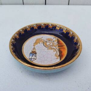 Vide poche, coupelle ou ramasse pièce en faïence de Longwy, à décor d'une lanterne  au bout d'une enseigne, émaux dorés. Certainement une commande spéciale d'un magasin ou hotel. Effet craquelé sur la céramique. Signée sur le dessous. Une micro égrenure sur le contour. Très bon état. Diamètre : 13,5 cm Hauteur : 3 cm