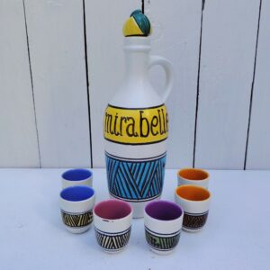 Service à liqueur mirabelle en céramique, par Elchinger datant des années 60, comprenant une bouteille et son bouchon à la forme de prune et de six verres à liqueur de différentes couleurs. Signé sur le dessous de la bouteille. Très bon état. Hauteur bouteille : 26,5 cm Hauteur et diamètre verre: 5 et 4 cm