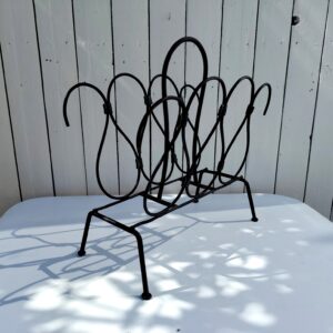 Porte revue en métal noir, attribué à Jacques Adnet, datant des années 50-60. Cuir sur les intersections des volutes, manque le cuir qui recouvrait la poignée. Petites traces d'usage. Un morceau de cuir se découd sur le haut. Bon état général Dimensions : 41,5 x 20 x 40 cm