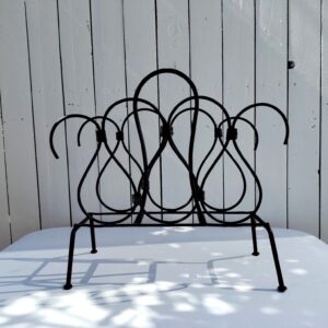 Porte revue en métal noir, attribué à Jacques Adnet, datant des années 50-60. Cuir sur les intersections des volutes, manque le cuir qui recouvrait la poignée. Petites traces d'usage. Un morceau de cuir se découd sur le haut. Bon état général Dimensions : 41,5 x 20 x 40 cm