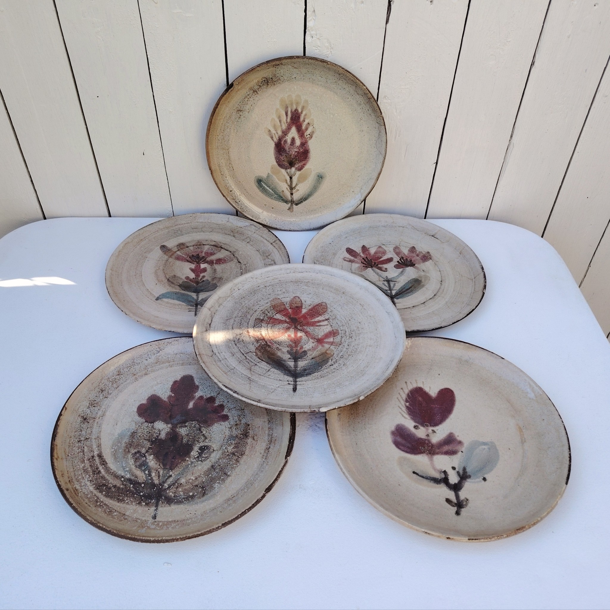 Six assiettes plates en céramique, au décor de fleur, par Gustave Reynaud atelier le mûrier Vallauris. Elles ont toutes un décor différent et façonnées différemment. Excellent état. Diamètre : 24 cm
