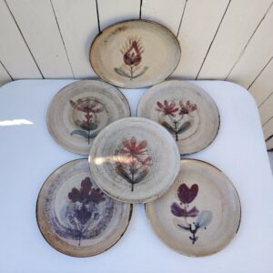 Six assiettes  plates en céramique, au décor de fleur, par Gustave Reynaud atelier le mûrier Vallauris. Elles ont toutes un décor différent et façonnées différemment. Excellent état. Diamètre : 24 cm