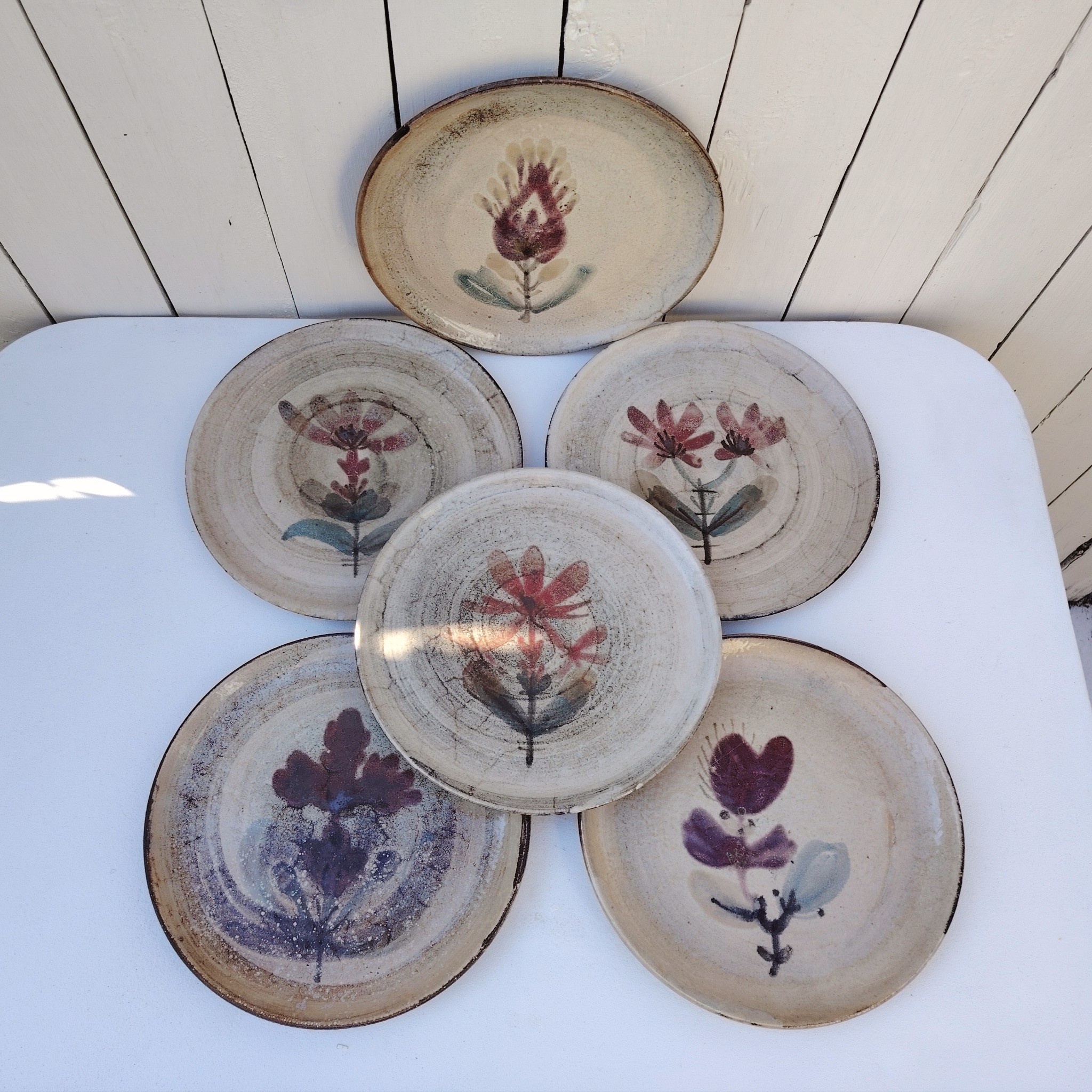 Six assiettes plates en céramique, au décor de fleur, par Gustave Reynaud atelier le mûrier Vallauris. Elles ont toutes un décor différent et façonnées différemment. Excellent état. Diamètre : 24 cm