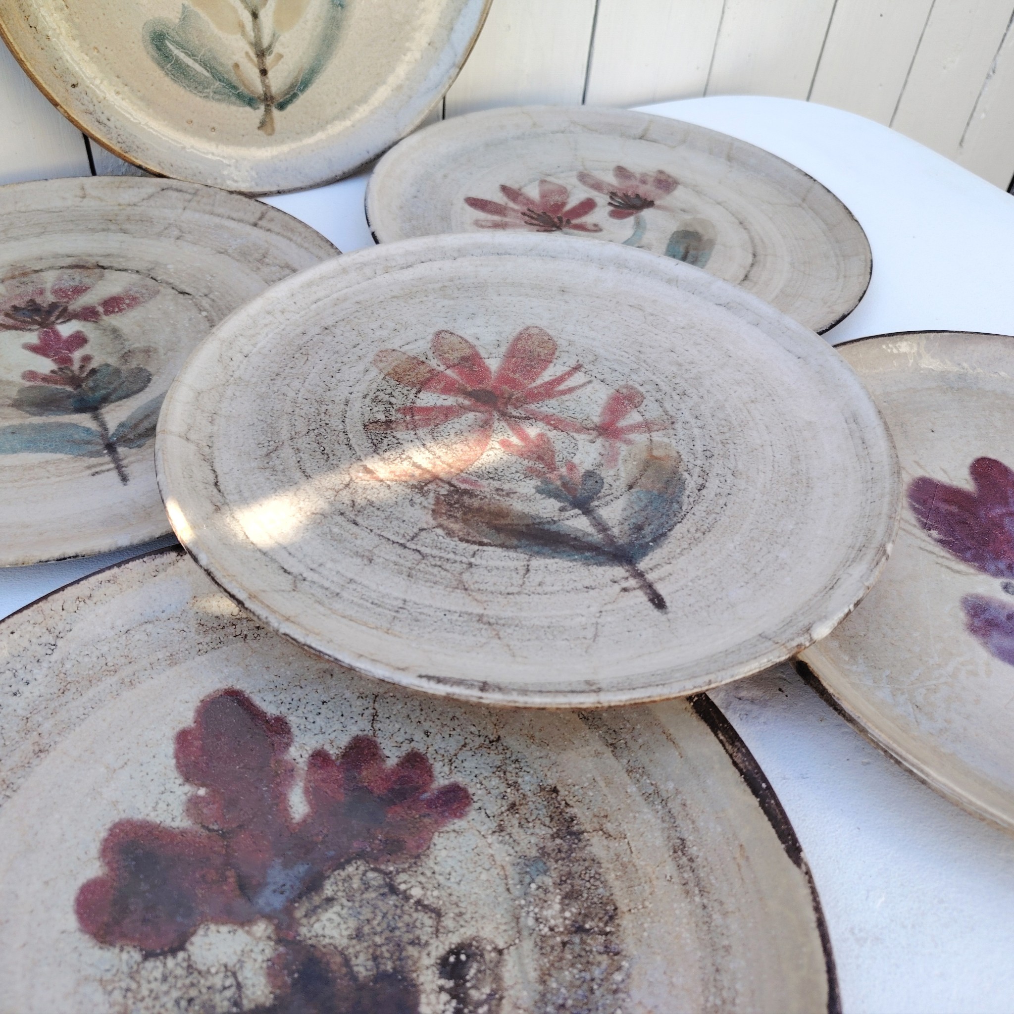 Six assiettes plates en céramique, au décor de fleur, par Gustave Reynaud atelier le mûrier Vallauris. Elles ont toutes un décor différent et façonnées différemment. Excellent état. Diamètre : 24 cm
