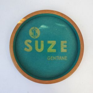 Ancien plateau de jeu publicitaire pour la marque suze. Entourage bois et intérieur en feutrine. Petites taches et un petit accroc, légèrement délavé. Bon état général. Diamètre : 31 cm