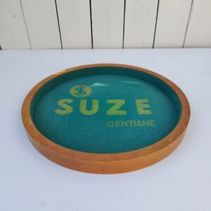 Ancien plateau de jeu publicitaire pour la marque suze. Entourage bois et intérieur en feutrine. Petites taches et un petit accroc, légèrement délavé. Bon état général. Diamètre : 31 cm