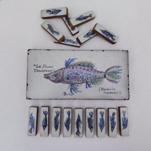Dessous de plat et 16 porte-couteaux à décor de poisson,en céramique par Michel Boillot, Signé sur le dessous de plat Des petits éclats sur le contour du dessous de plat, petites égrenures sur les porte-couteaux  Bon état général. Dimensions dessous de plat : 25 x 12 cm Dimensions porte-couteau : 7 x 2 cm