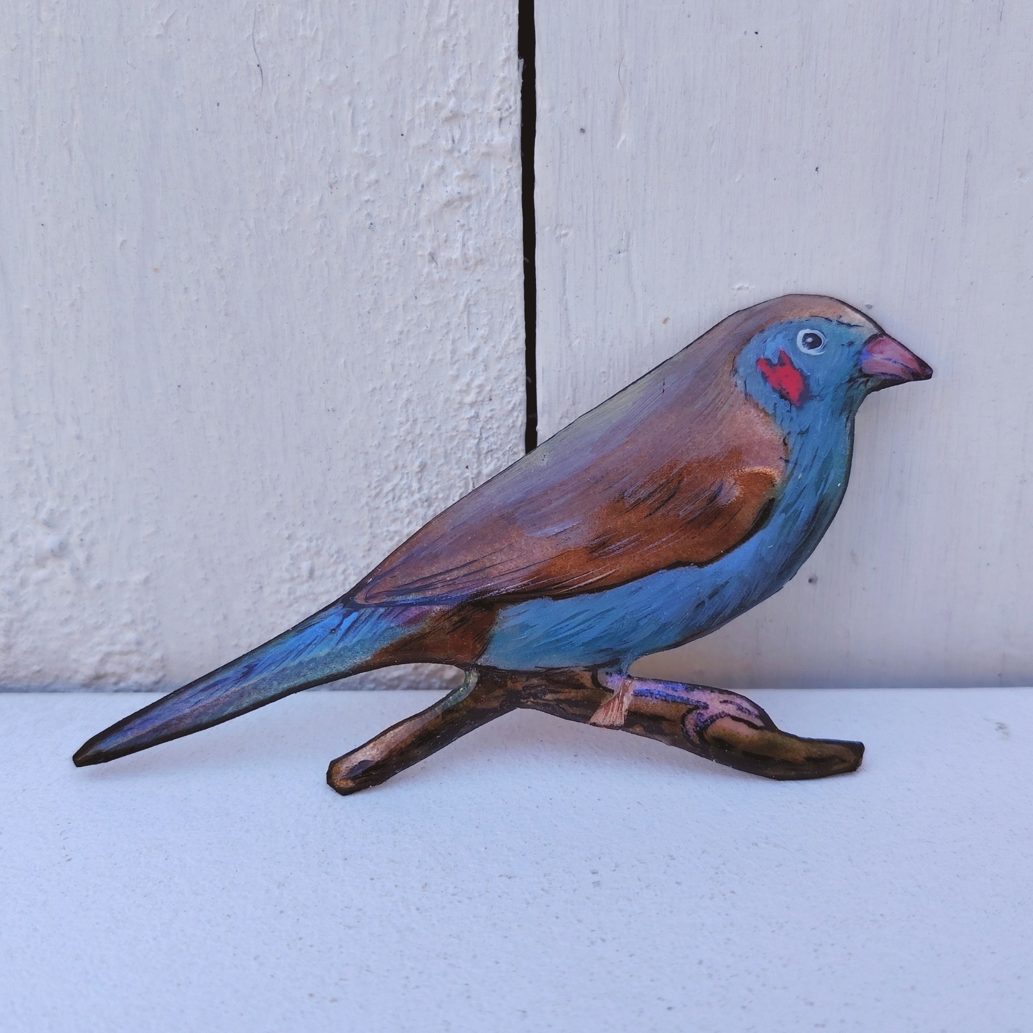 Oiseau représentant un cordon bleu à joues rouges, en émaux de Limoges sur cuivre. Datant des années 60-70. Un éclat d'émail sur la branche. Ne possède pas de point d'accroche. Bon état général. Dimensions : 11,5 x 5,5 cm