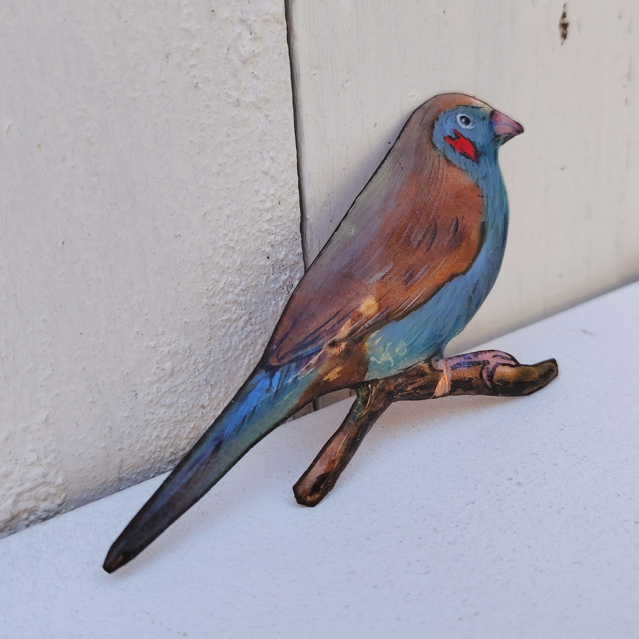 Oiseau représentant un cordon bleu à joues rouges, en émaux de Limoges sur cuivre. Datant des années 60-70. Un éclat d'émail sur la branche. Ne possède pas de point d'accroche. Bon état général. Dimensions : 11,5 x 5,5 cm