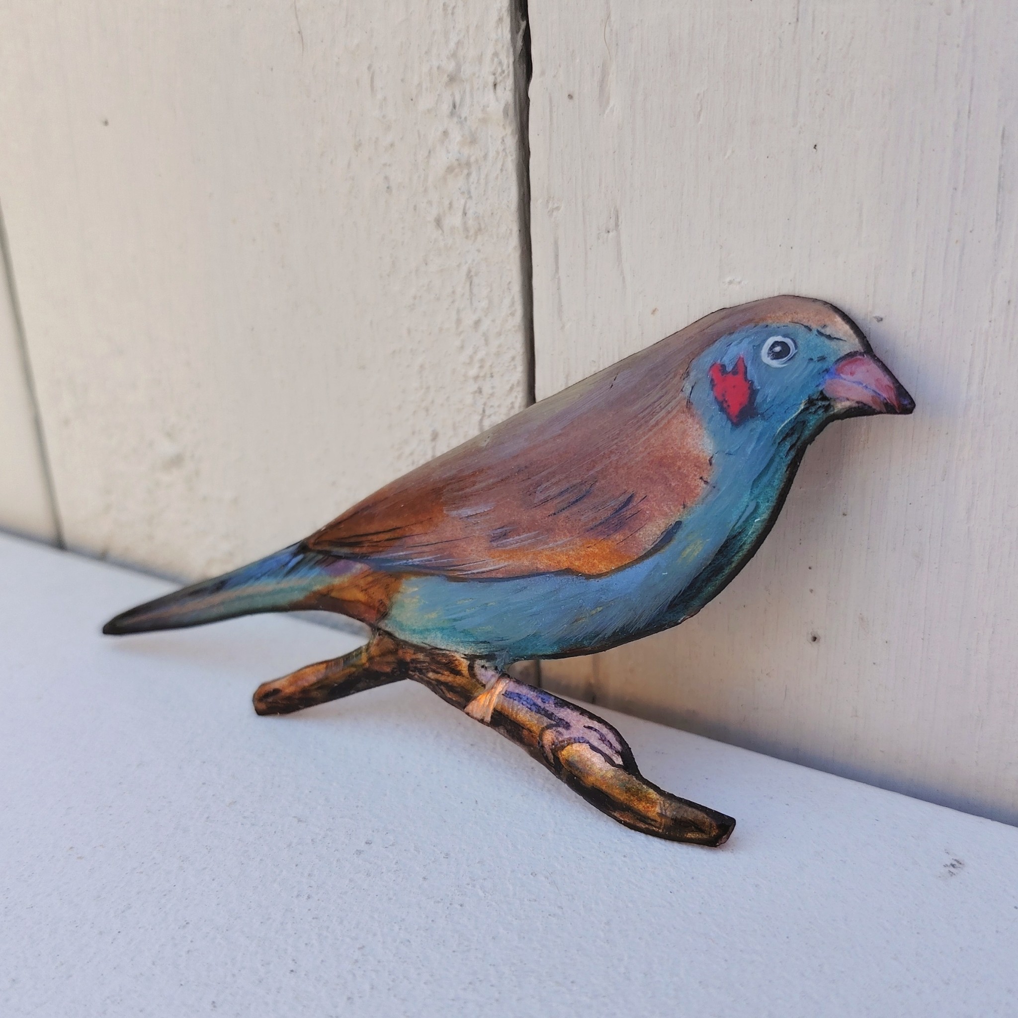 Oiseau représentant un cordon bleu à joues rouges, en émaux de Limoges sur cuivre. Datant des années 60-70. Un éclat d'émail sur la branche. Ne possède pas de point d'accroche. Bon état général. Dimensions : 11,5 x 5,5 cm
