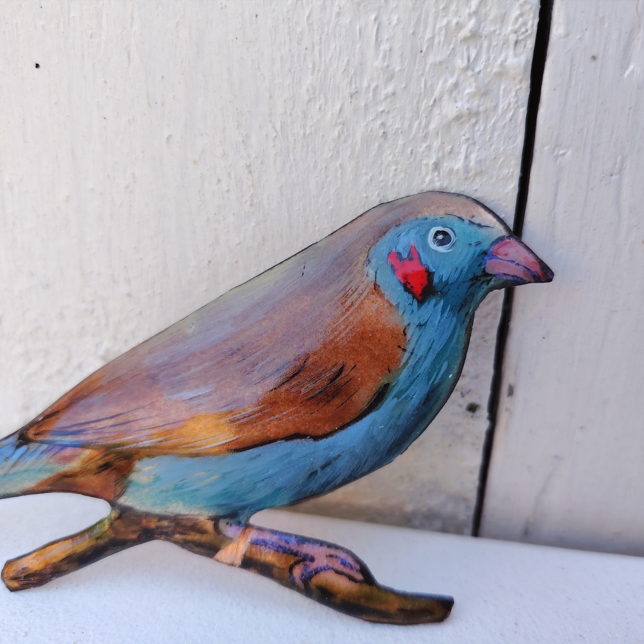 Oiseau représentant un cordon bleu à joues rouges, en émaux de Limoges sur cuivre. Datant des années 60-70. Un éclat d'émail sur la branche. Ne possède pas de point d'accroche. Bon état général. Dimensions : 11,5 x 5,5 cm