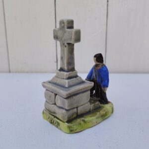 Sujet en céramique de Quimper représentant un breton devant un calvaire, signé Nik. La croix a été cassée/recollée à sa base, un éclat sur le ruban du chapeau. Bon état. Hauteur : 9,5 cm