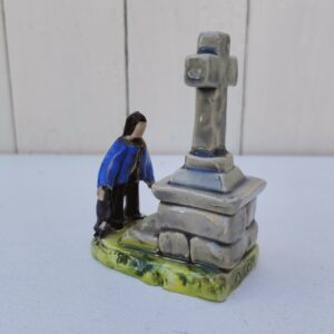 Sujet en céramique de Quimper représentant un breton devant un calvaire, signé Nik. La croix a été cassée/recollée à sa base, un éclat sur le ruban du chapeau. Bon état. Hauteur : 9,5 cm