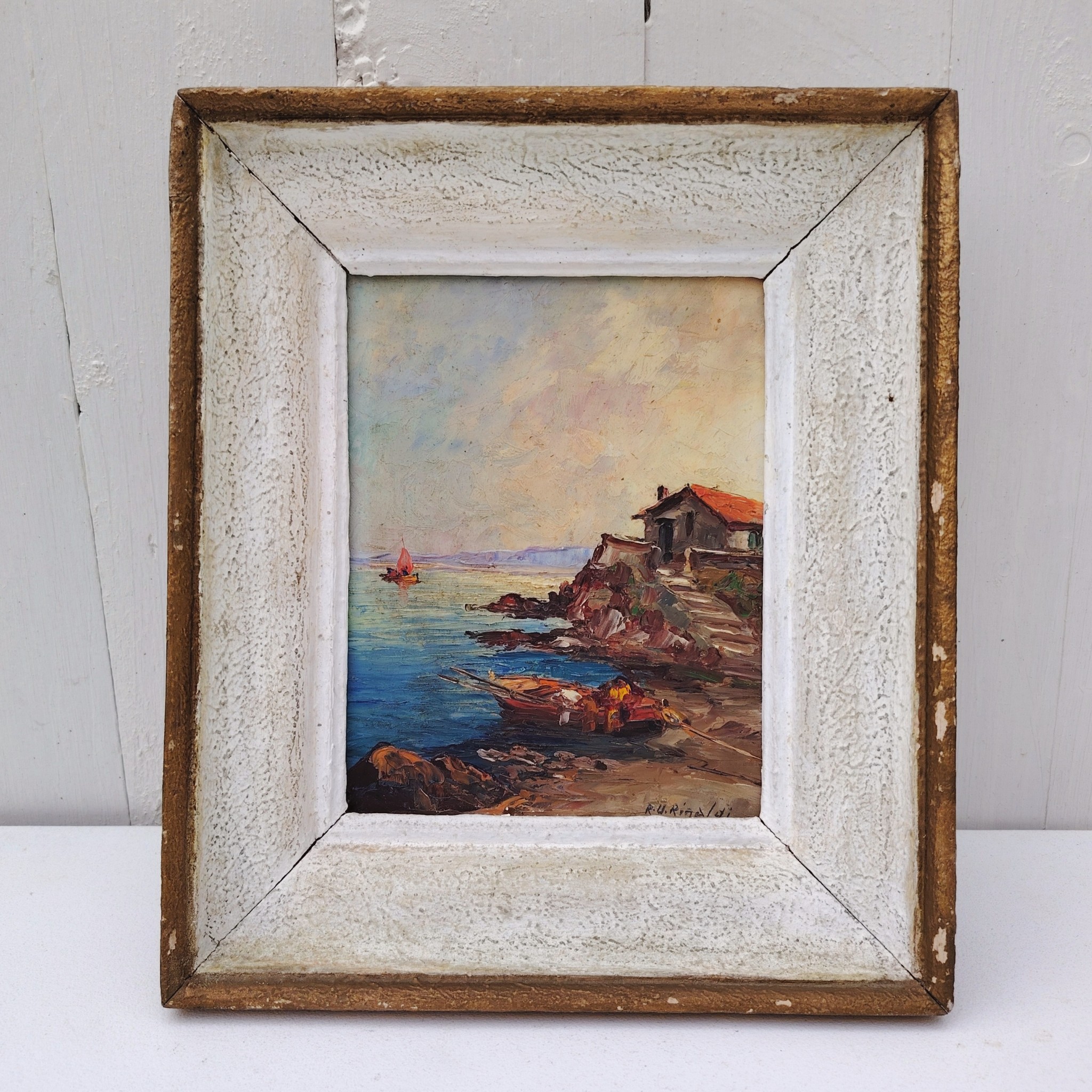 Huile sur panneau isorel représentant un bateau amarré dans une crique en premier plan , en deuxième plan une maison de pêcheur sur une hauteur et dans le fond on distingue une falaise et un voilier naviguant. Cadre en bois cérusé blanc. Signé RU Rinaldi en bas à droite. Bon état général. Dimensions cadre : 22 x 25,5 cm