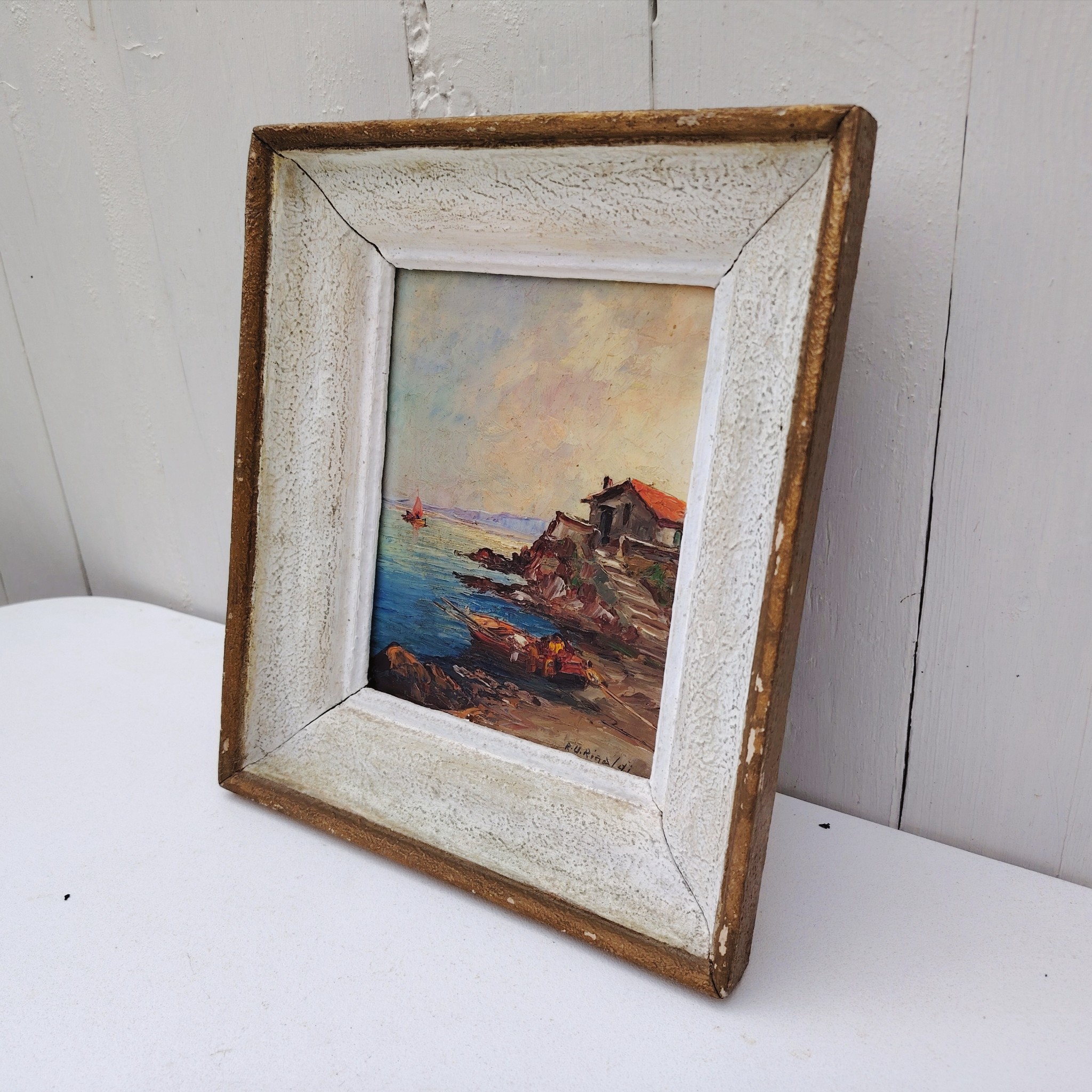 Huile sur panneau isorel représentant un bateau amarré dans une crique en premier plan , en deuxième plan une maison de pêcheur sur une hauteur et dans le fond on distingue une falaise et un voilier naviguant. Cadre en bois cérusé blanc. Signé RU Rinaldi en bas à droite. Bon état général. Dimensions cadre : 22 x 25,5 cm