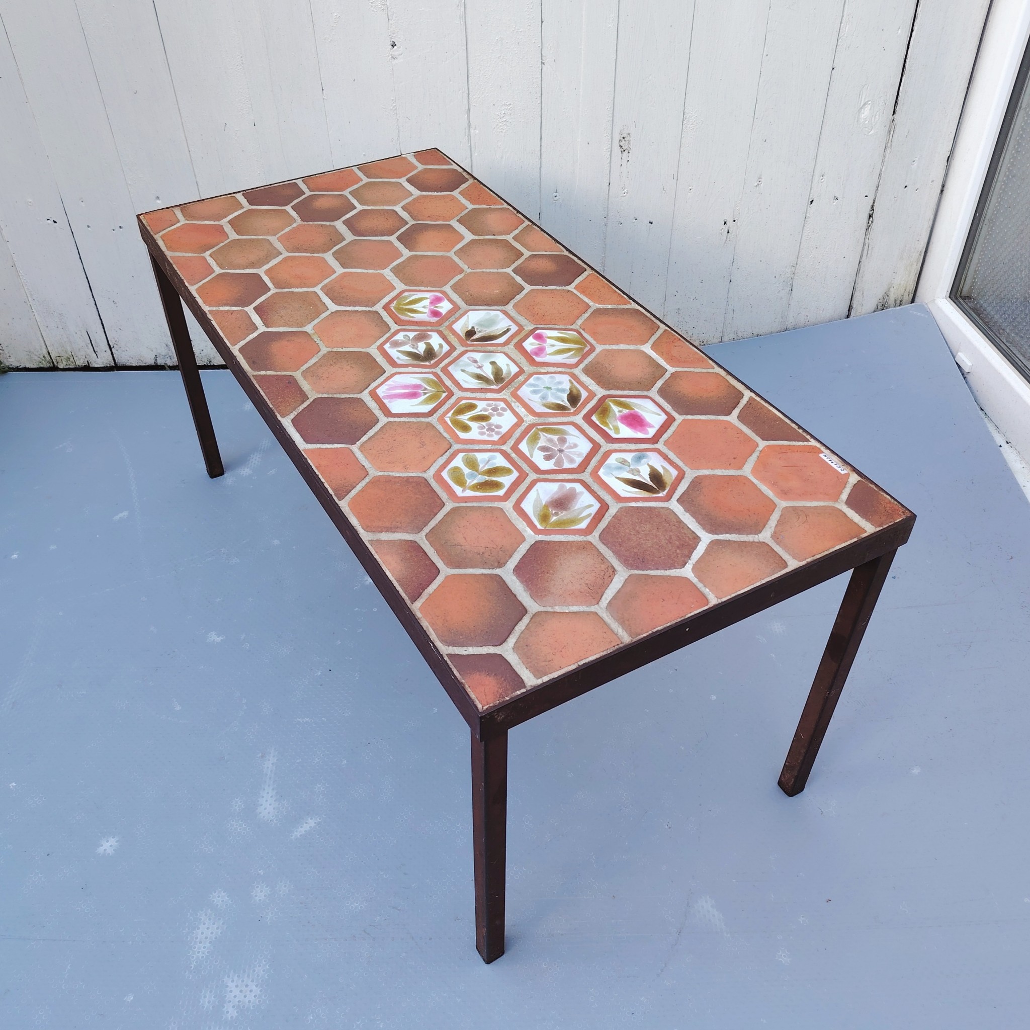Table basse par Roger Capron à Vallauris. Piétement en métal noir, plateau en tomettes provençales et céramique à fleur. Modèle peu commun. Signé sur la table . Quelques traces et rayures d'usage. Très bon état. Hauteur : 39 cm dimensions plateau : 82,5 x 39,5 cm