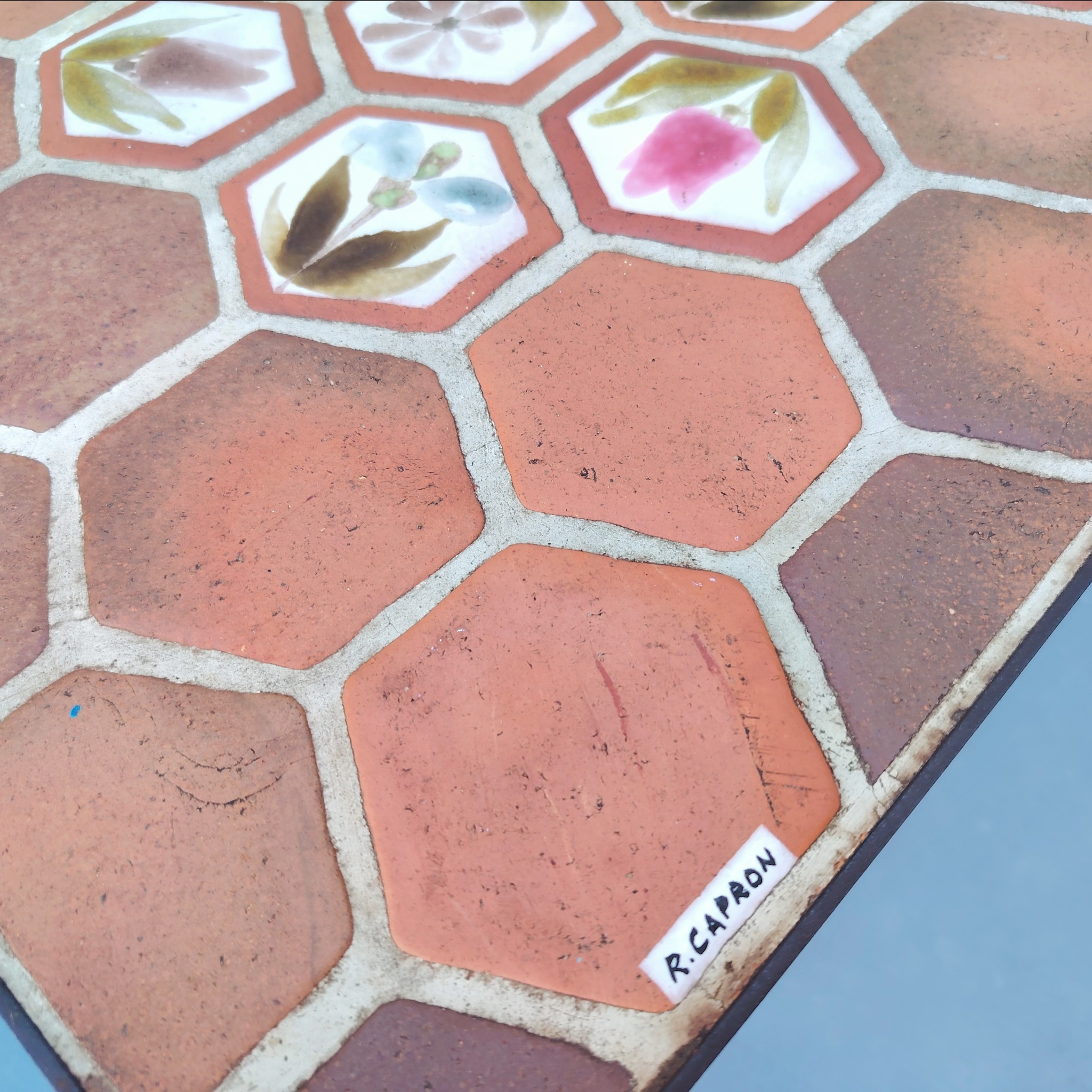 Table basse par Roger Capron à Vallauris. Piétement en métal noir, plateau en tomettes provençales et céramique à fleur. Modèle peu commun. Signé sur la table . Quelques traces et rayures d'usage. Très bon état. Hauteur : 39 cm dimensions plateau : 82,5 x 39,5 cm