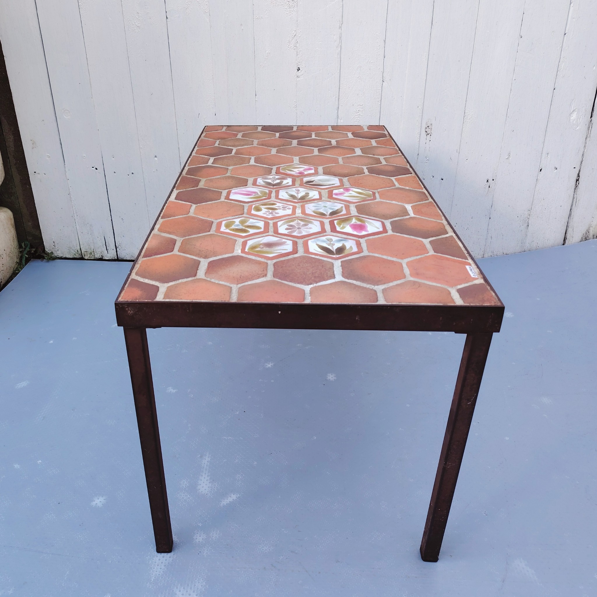 Table basse par Roger Capron à Vallauris. Piétement en métal noir, plateau en tomettes provençales et céramique à fleur. Modèle peu commun. Signé sur la table . Quelques traces et rayures d'usage. Très bon état. Hauteur : 39 cm dimensions plateau : 82,5 x 39,5 cm