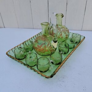 Service à liqueur en cristal de Baccarat . Le service est composé de 10 tasses à liqueur, de deux carafes et d'un plateau. Cristal teinté vert avec dorure. Non estampillé car datant d'avant 1936. Petites rayures d'usage. Petits féles sur trois tasses au niveau de l'anse. Petits manques de dorure sur le contour du plateau. Bon état général. Dimension plateau : 29 cm x 20,5 cm Hauteur Tasse : 3 cm Diamètre tasse : 3,5 cm Hauteur Carafe : 13,5 cm