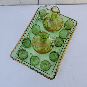 Service à liqueur en cristal de Baccarat . Le service est composé de 10 tasses à liqueur, de deux carafes et d'un plateau. Cristal teinté vert avec dorure. Non estampillé car datant d'avant 1936. Petites rayures d'usage. Petits féles sur trois tasses au niveau de l'anse. Petits manques de dorure sur le contour du plateau. Bon état général. Dimension plateau : 29 cm x 20,5 cm Hauteur Tasse : 3 cm Diamètre tasse : 3,5 cm Hauteur Carafe : 13,5 cm