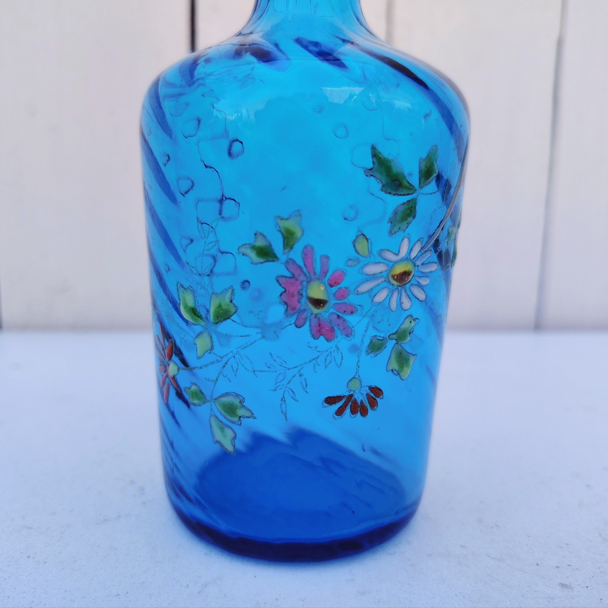 Ancienne bouteille en verre  torsadé de couleur bleu à décor frise florale émaillée Très bon état. Hauteur  : 17 cm