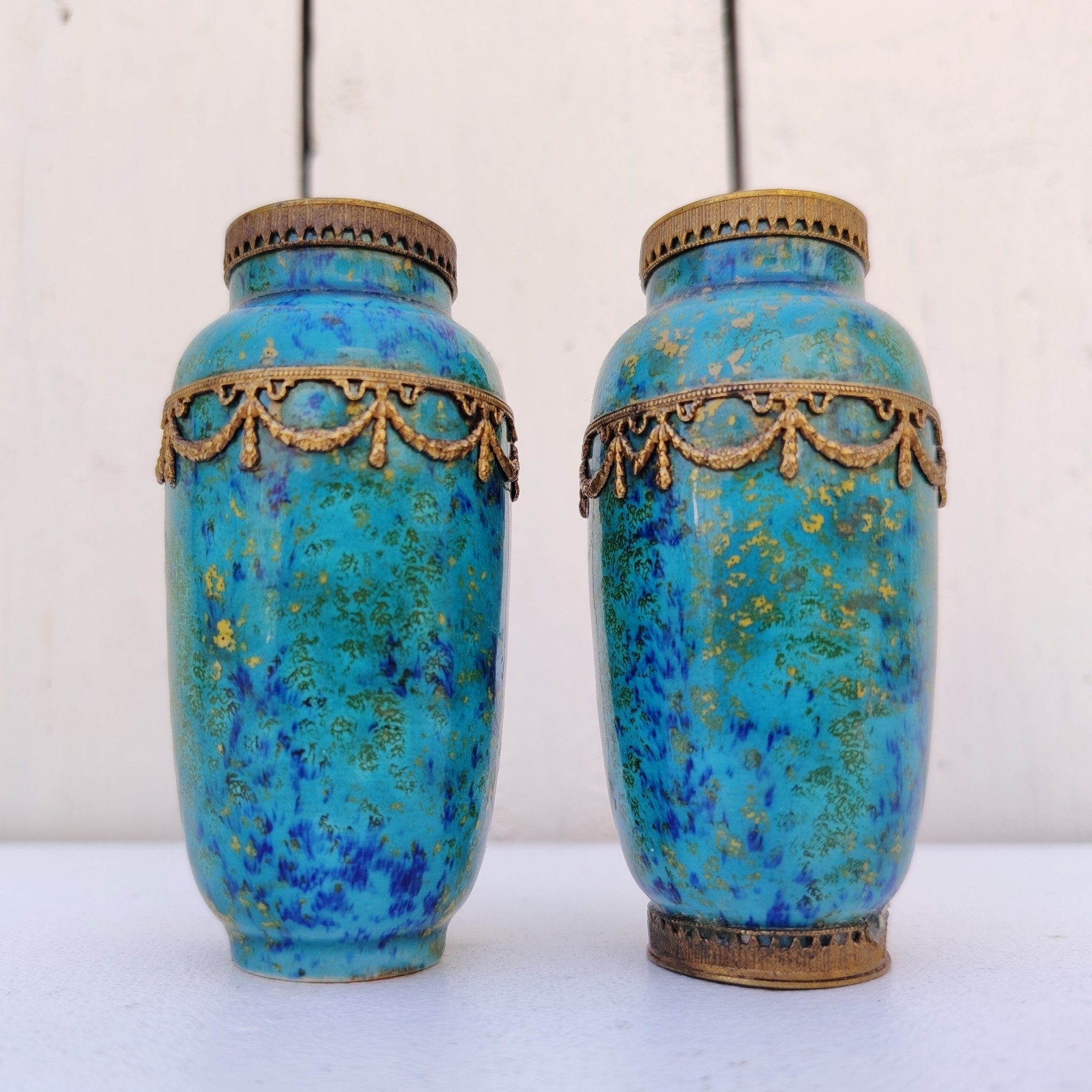 Paires de vases miniatures art déco attribués à Paul Millet, en céramique de sèvres. Dans les tons bleus avec des touches de doré. Un cachet sur le dessous.  Manque le cerclage bronze au pied d'un vase. Bon état général. Hauteur : 8,5 cm