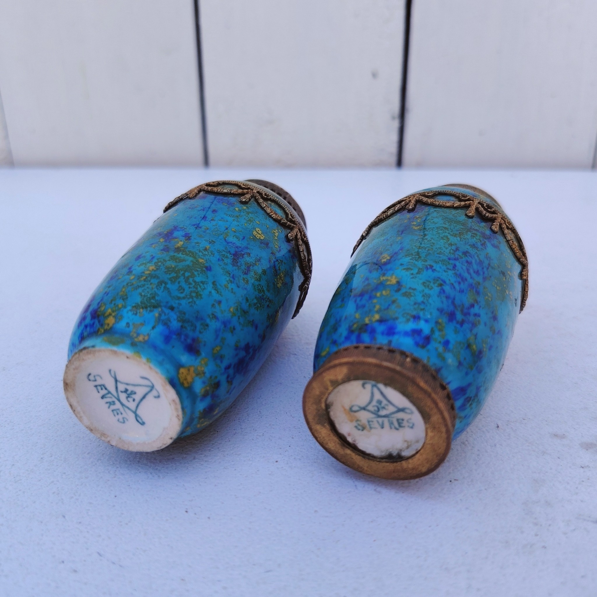 Paires de vases miniatures art déco attribués à Paul Millet, en céramique de sèvres. Dans les tons bleus avec des touches de doré. Un cachet sur le dessous.  Manque le cerclage bronze au pied d'un vase. Bon état général. Hauteur : 8,5 cm