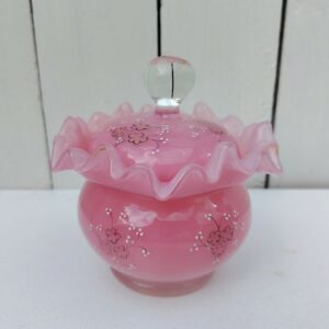 Pot couvert pouvant servir de baguier ou autre en verre soufflé de couleur rose, collerette torsadée. Décor de fleur rehaussé de points émaillés blancs en relief. Les fleurs et la prise du couvercle devait être certainement doré car on y voit encore le petites de la dorure. Un petit éclat sur l'intérieur du couvercle non visible quand il est fermé, et traces blanches sur le talon du pot non visible quand il est posé. Bon état général Hauteur avec couvercle : 13 cm Diamètre : 11 cm