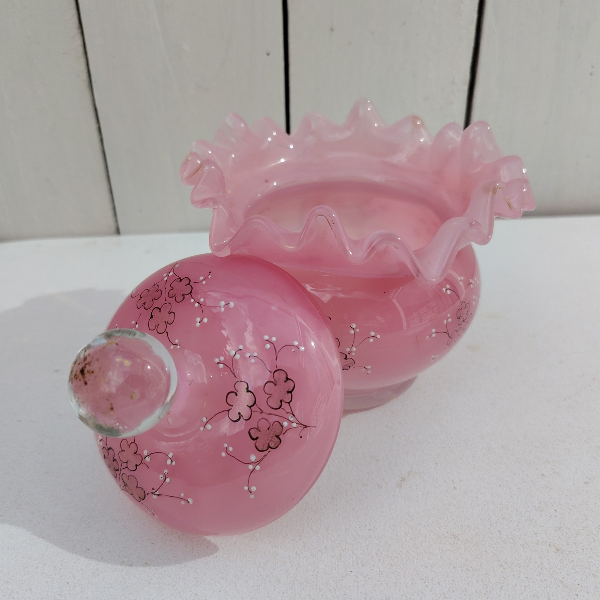 Pot couvert pouvant servir de baguier ou autre en verre soufflé de couleur rose, collerette torsadée. Décor de fleur rehaussé de points émaillés blancs en relief. Les fleurs et la prise du couvercle devait être certainement doré car on y voit encore le petites de la dorure. Un petit éclat sur l'intérieur du couvercle non visible quand il est fermé, et traces blanches sur le talon du pot non visible quand il est posé. Bon état général Hauteur avec couvercle : 13 cm Diamètre : 11 cm