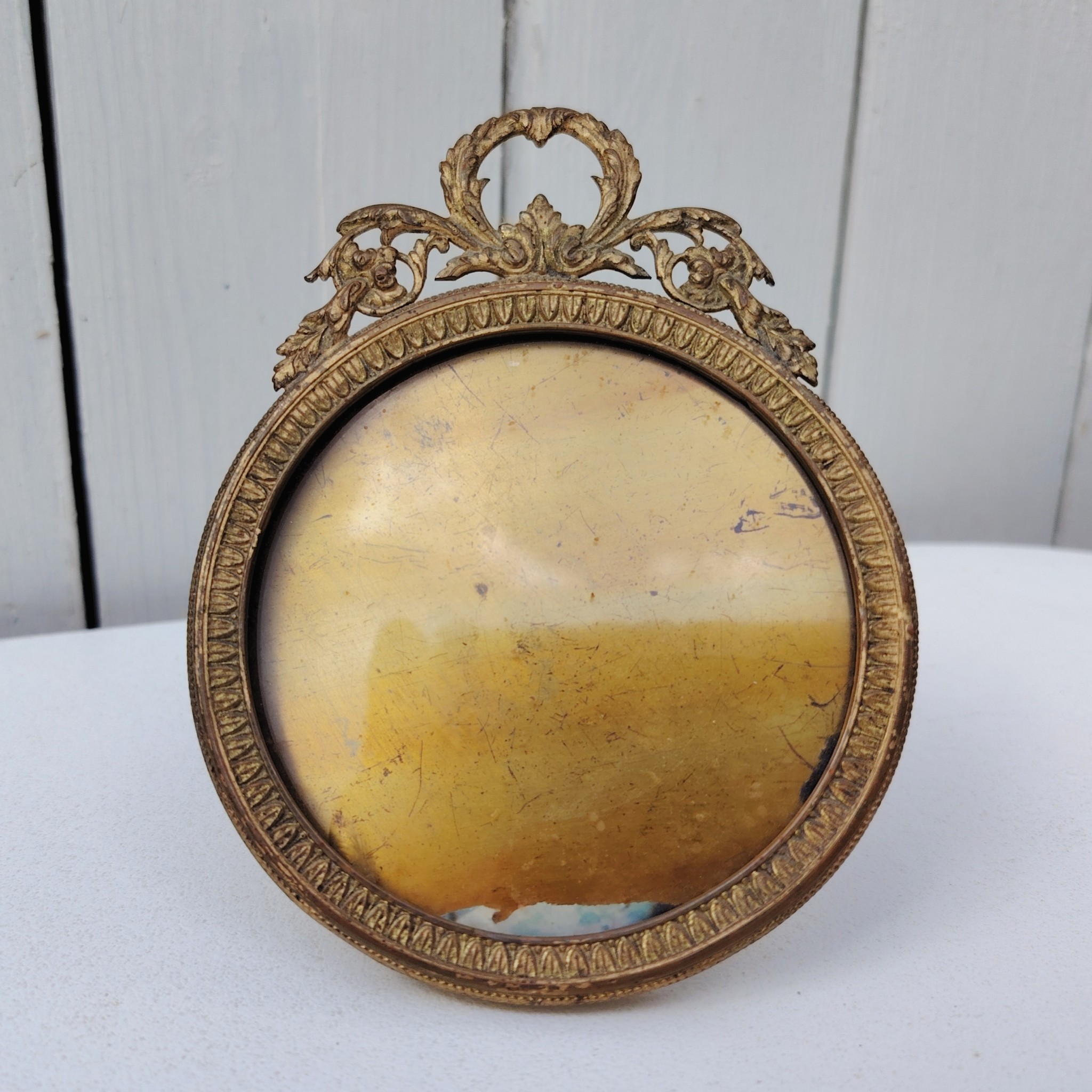 Cadre photo chevalet en bronze doré, style Louis XVI, Ruban sur le haut. Une trace de photo collée sur le rebord intérieur. Bon état général Diamètre : 9 cm