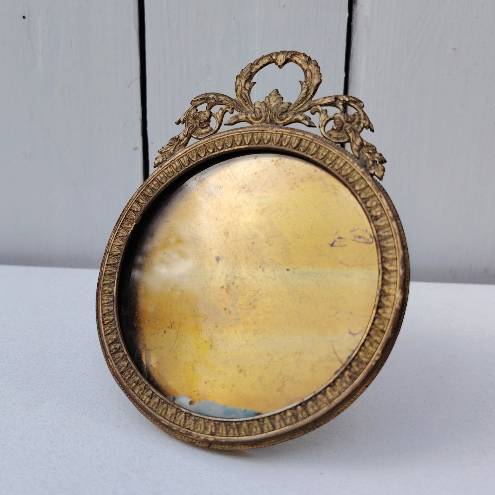 Cadre photo chevalet en bronze doré, style Louis XVI, Ruban sur le haut. Une trace de photo collée sur le rebord intérieur. Bon état général Diamètre : 9 cm