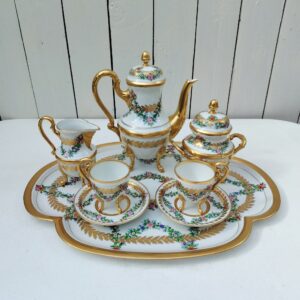 Service à café tête à tête en porcelaine de Limoges, comprenant le plateau, la cafetière, les deux tasses avec soucoupes, le pot à lait et le sucrier. Décor floral orné de dorure. Estampillé Porcelaine de limoge avec les initiales du décorateur sous le plateau . Excellent état . Dimensions : Hauteur cafetière : 20,5 cm Hauteur sucrier avec couvercle : 14 cm Hauteur pot à lait : 11,5 cm Hauteur tasse : 8,5 cm diamètre tasse : 5,7 cm diamètre soucoupe : 11,5  Dimensions plateau : 40,5 x 30,5 cm