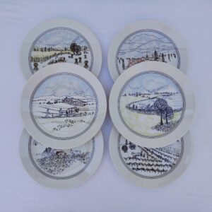 Six assiettes à dessert en porcelaine d'Auteuil, paysages naïf, décor créé par Danielle Dillemann. Six décors différents, légères traces d'usage. Très bon état. Diamètre : 19 cm