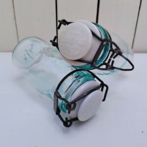 Paire d'anciens pots en verre de la marque L'idéale, bouchon en porcelaine. Système de fermeture comme les pots Le parfait. Très bon état. Hauteur : 15,5 cm