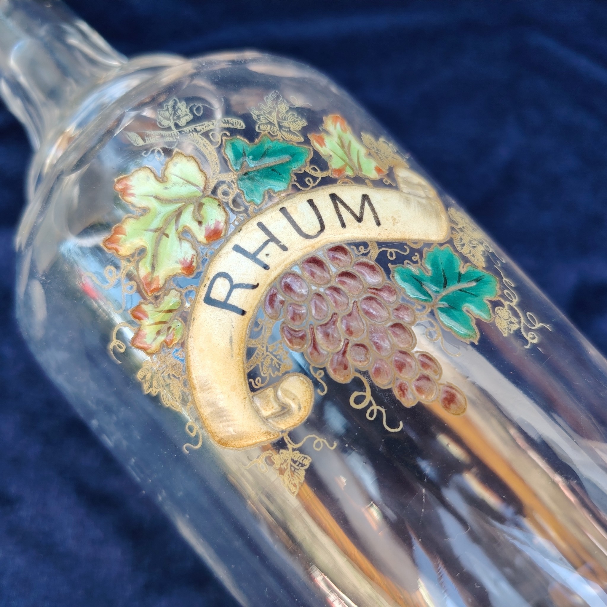 Ancienne bouteille en verre taillé à facette, décor émaillé en relief, marqué Rhum. (Idéale pour faire son rhum arrangé) Des petites traces de calcaire et traces d'usage. Bon état général Hauteur : 30 cm