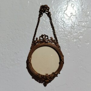 Petit cadre photo mural en bronze doré et bois, style Louis XVI, noeud ruban sur le haut. Chaînette pour pouvoir l'accrocher au mur Petites rayures sur le verre Bon état général Diamètre : 5,5 cm Hauteur avec chaînette : 13 cm