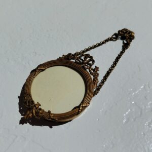 Petit cadre photo mural en bronze doré et bois, style Louis XVI, noeud ruban sur le haut. Chaînette pour pouvoir l'accrocher au mur Petites rayures sur le verre Bon état général Diamètre : 5,5 cm Hauteur avec chaînette : 13 cm
