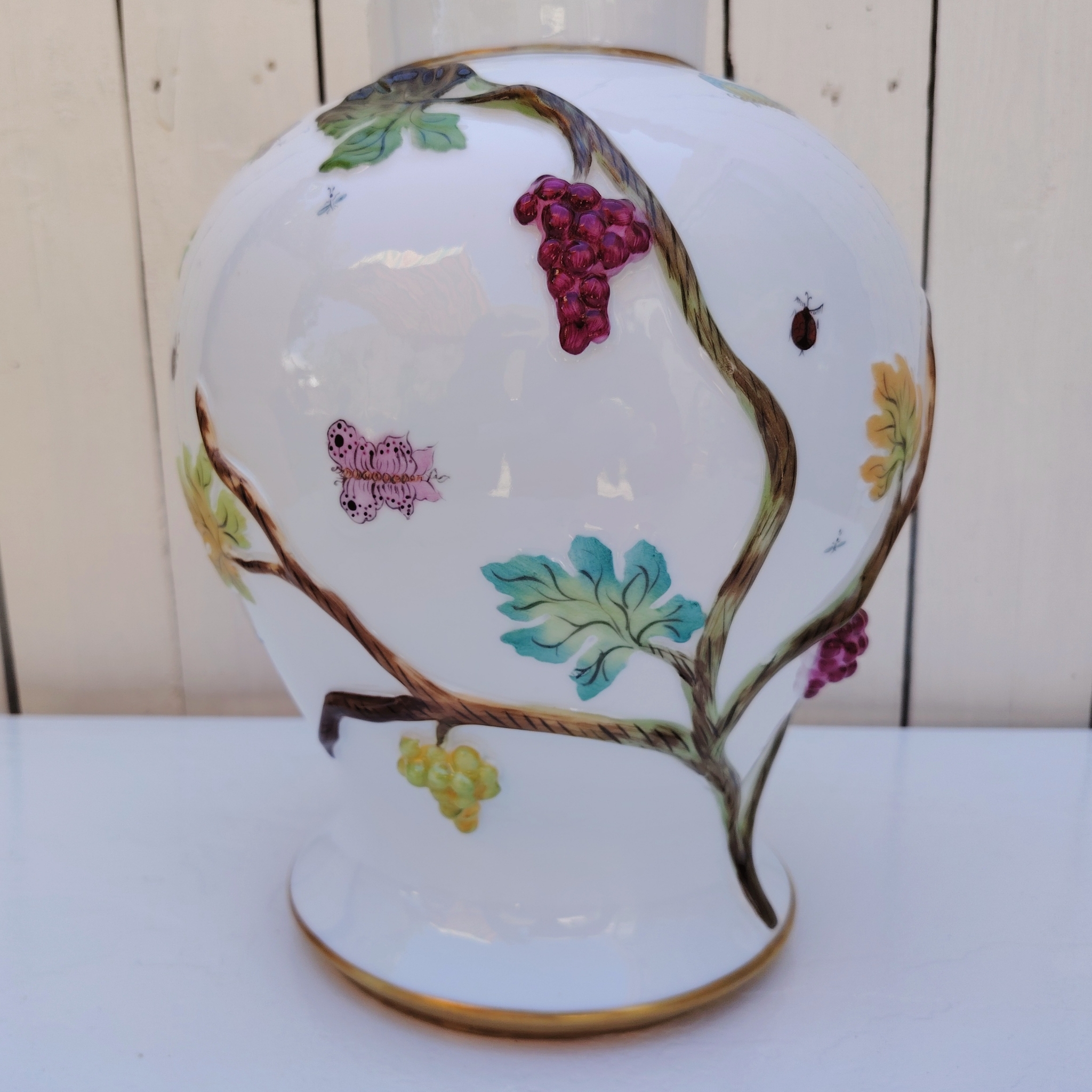 Grand pot couvert en porcelaine portugaise Pac. Orné de vignes et grappes de raisins en relief, et de papillons et coccinelles peints. Liseré doré, poignée du couvercle représentant une branche dorée surhaussé d'un perroquet. Très belle facture. Excellent état.  Hauteur avec couvercle : ~47 cm