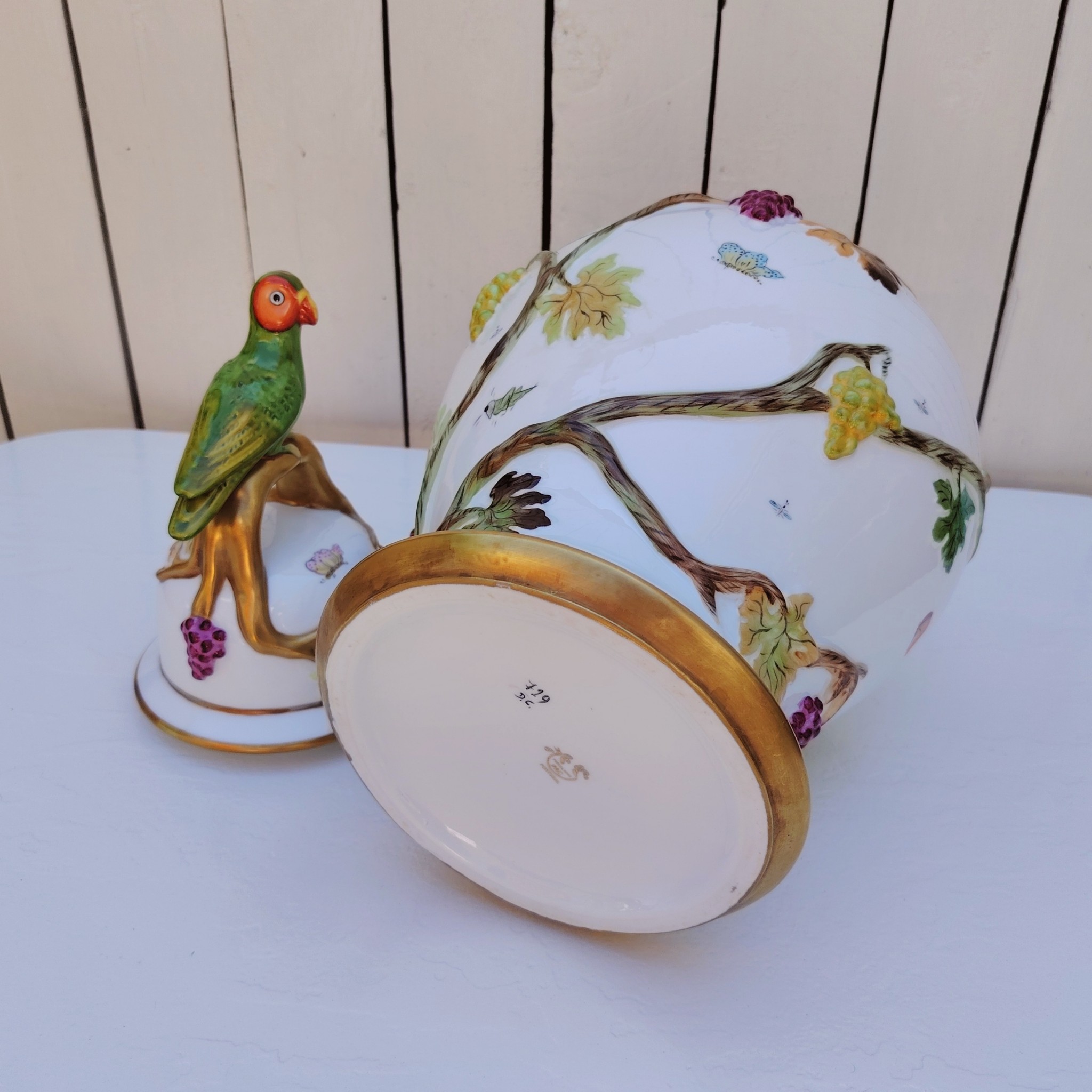 Grand pot couvert en porcelaine portugaise Pac. Orné de vignes et grappes de raisins en relief, et de papillons et coccinelles peints. Liseré doré, poignée du couvercle représentant une branche dorée surhaussé d'un perroquet. Très belle facture. Excellent état.  Hauteur avec couvercle : ~47 cm
