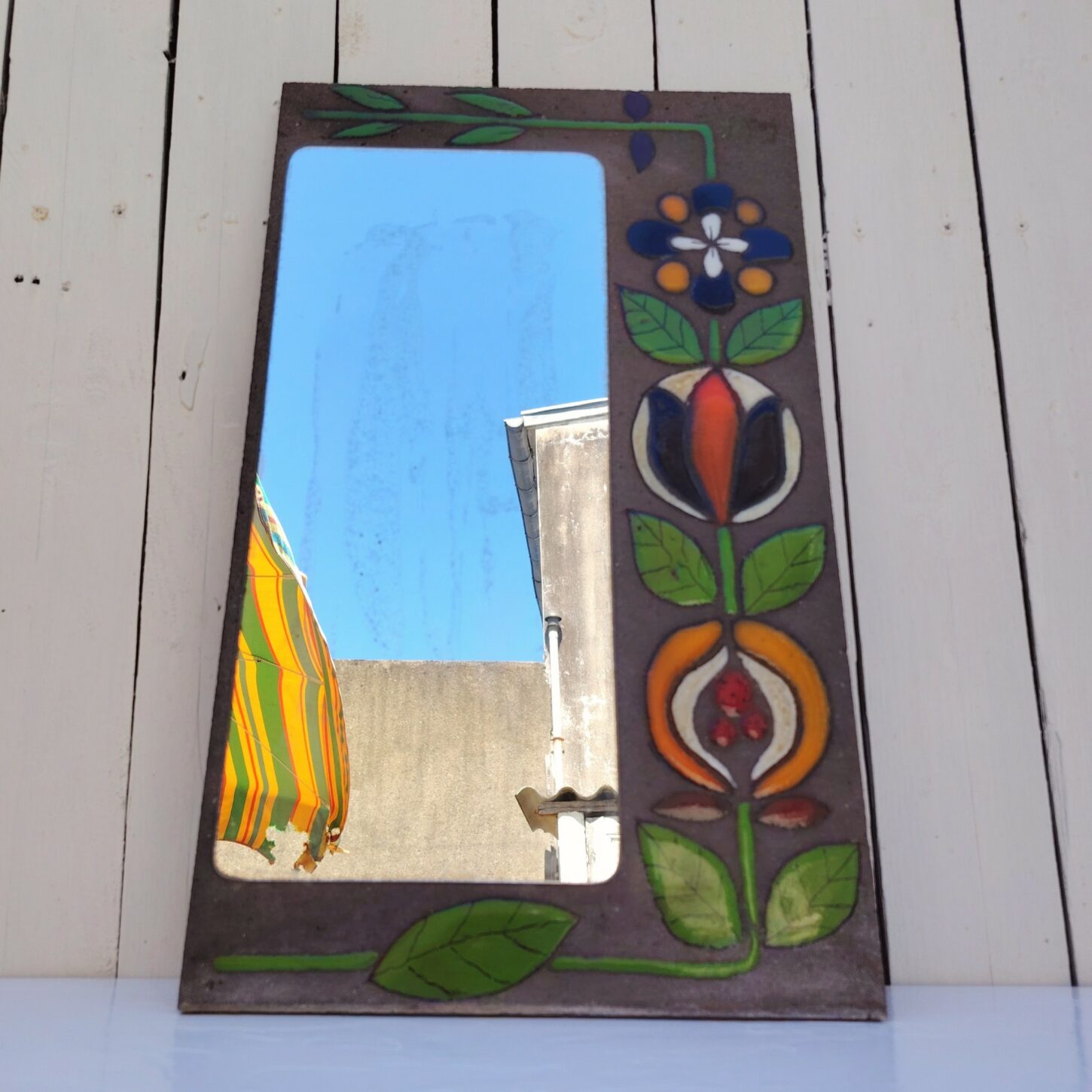 Miroir à poser en pierre de lave avec fleurs colorées émaillées, traces sur le miroir probablement la colle que l'on voit au travers. Très bel objet déco. Bon état général. Dimensions : 50 x 30 cm