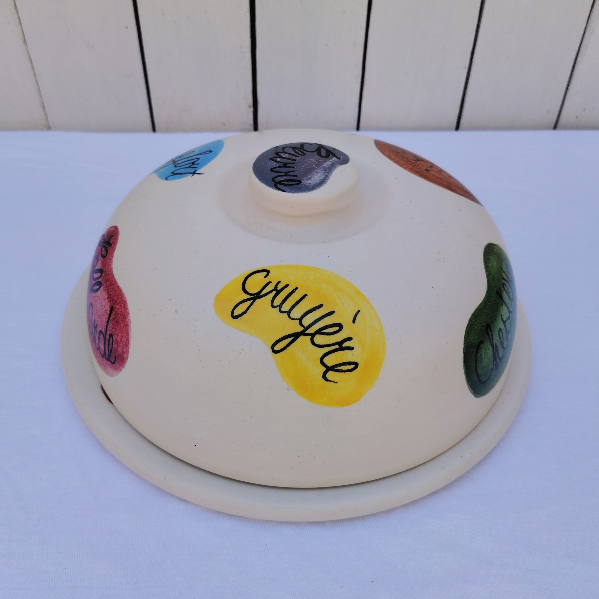 Plateau et cloche à fromage en céramique datant des années 60, par Elchinger. Plusieurs noms de fromages sur la cloche et le plateau. Des petites rayures d'usage, Signé sur le dessous. Bon état général . Hauteur avec cloche : 14,5 cm Diamètre : 28,5 cm
