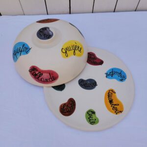Plateau et cloche à fromage en céramique datant des années 60, par Elchinger. Plusieurs noms de fromages sur la cloche et le plateau. Des petites rayures d'usage, Signé sur le dessous. Bon état général . Hauteur avec cloche : 14,5 cm Diamètre : 28,5 cm