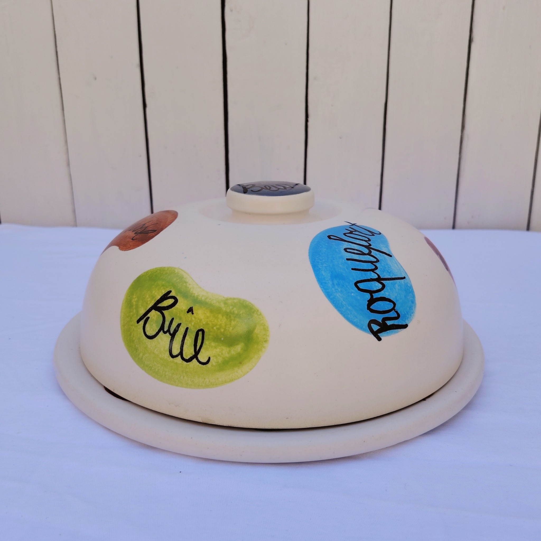 Plateau et cloche à fromage en céramique datant des années 60, par Elchinger. Plusieurs noms de fromages sur la cloche et le plateau. Des petites rayures d'usage, Signé sur le dessous. Bon état général . Hauteur avec cloche : 14,5 cm Diamètre : 28,5 cm