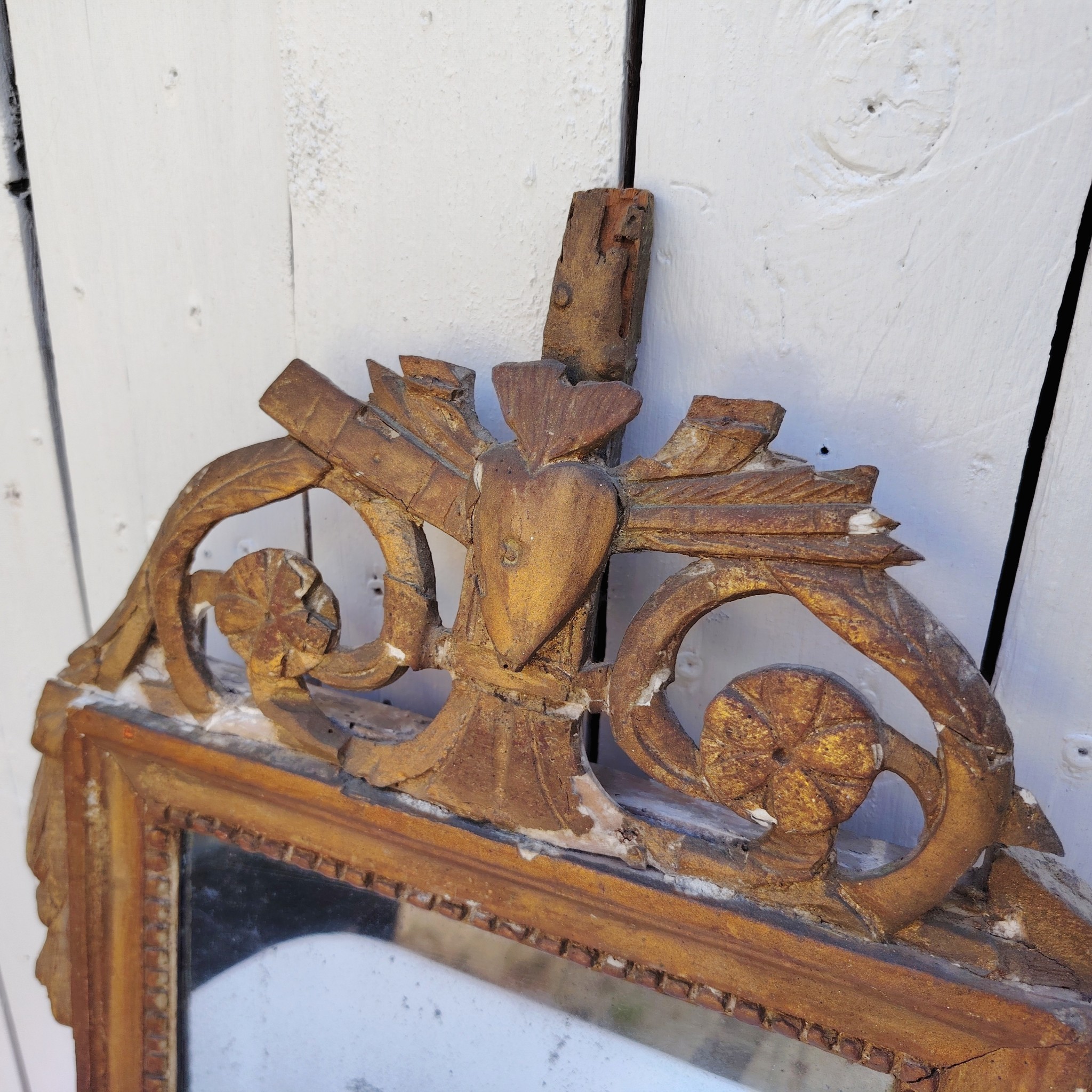 Ancien miroir en bois et stuc doré, de style Louis XVI, fin XVIIIéme début XIXéme. Fronton à enroulement de feuillage orné d'un coeur en son centre. Manque une partie du fronton, des éclats et maque de dorure. Tain terni et taché. Dans son jus Dimensions : 54 x 33 x 4 cm