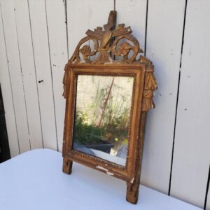 Ancien miroir en bois et stuc doré, de style Louis XVI, fin XVIIIéme début XIXéme. Fronton à enroulement de feuillage orné d'un coeur en son centre. Manque une partie du fronton, des éclats et maque de dorure. Tain terni et taché. Dans son jus Dimensions : 54 x 33 x 4 cm